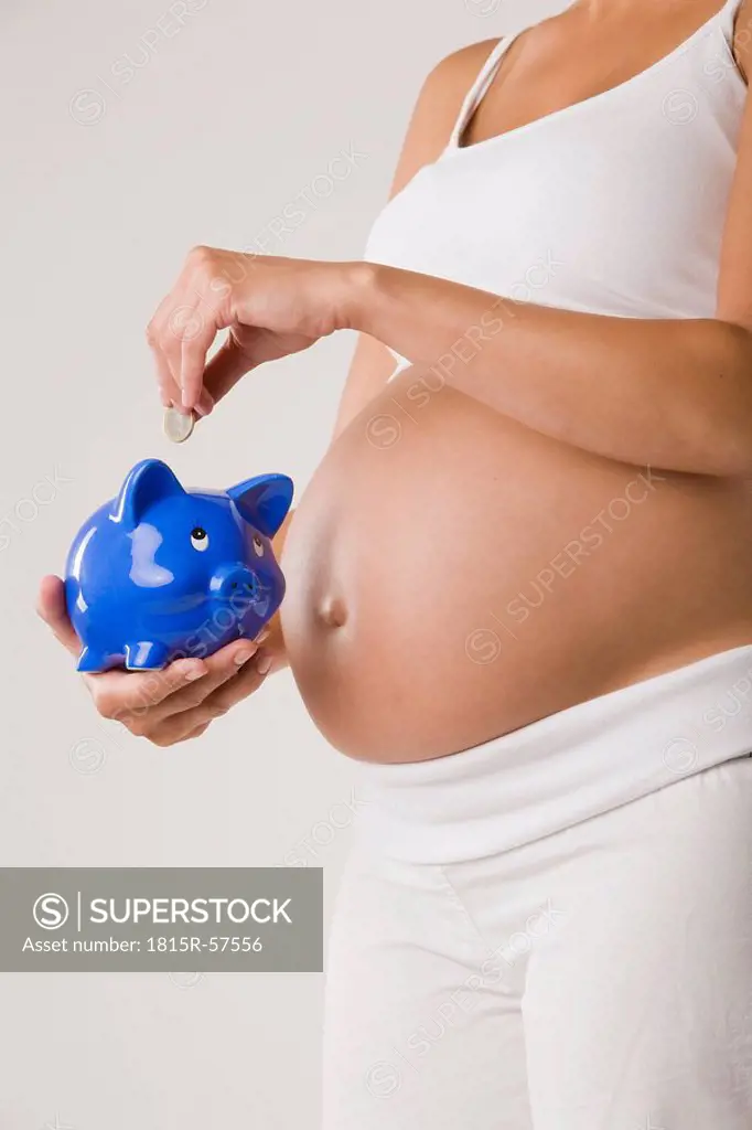 Pregnant woman putting Euro coin in piggy bank, mid section