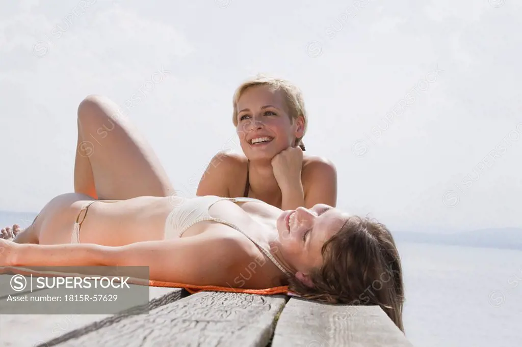 Germany, Bavaria, Two young women lying on jetty, smiling, portrait