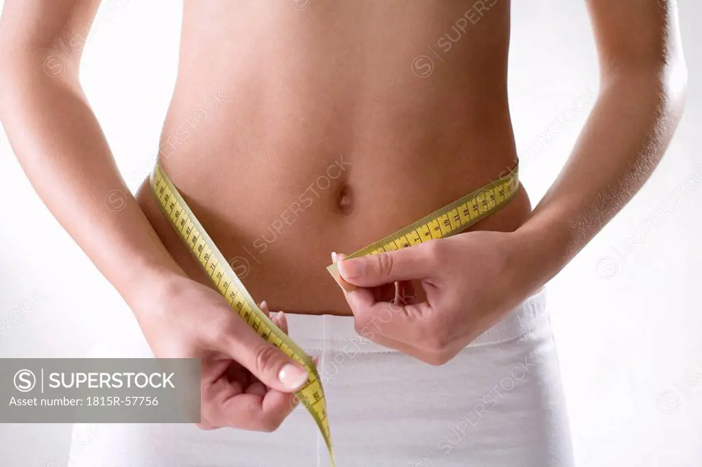 Young woman checking her waistline with measuring tape