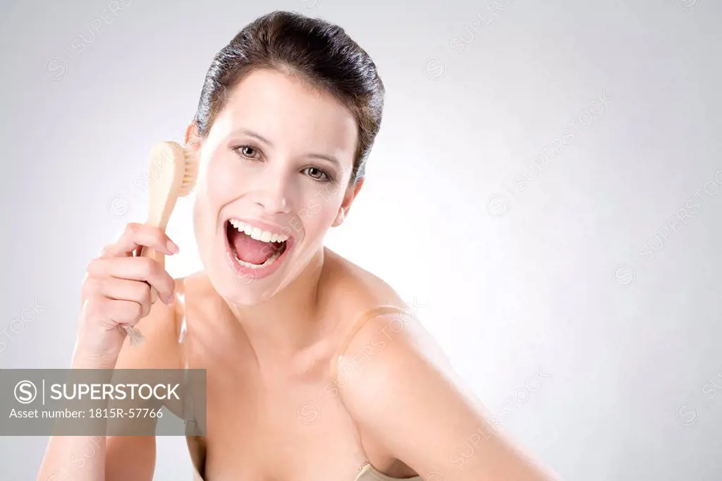 Young woman using peeling brush, laughing, close up