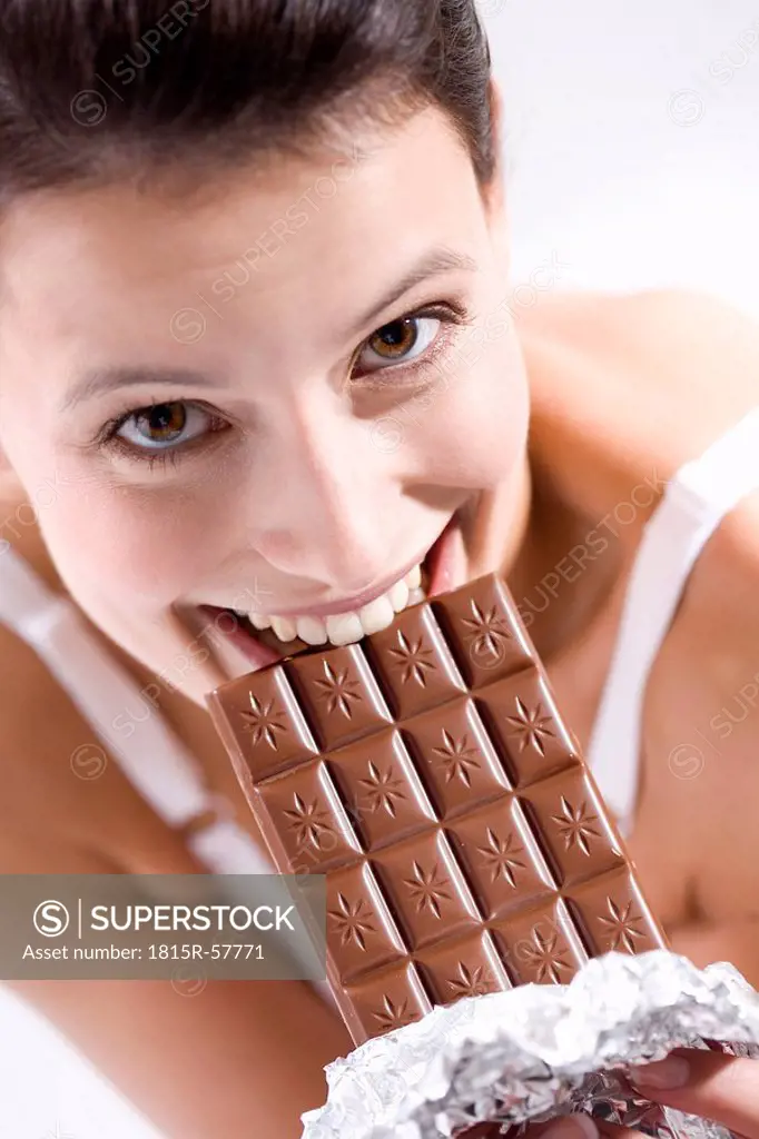 Young woman biting into chocolate bar, smiling