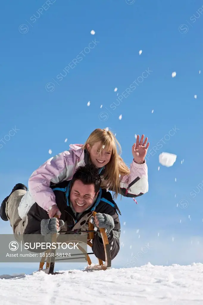 Germany, Bavaria, Couple lying on sled, having fun