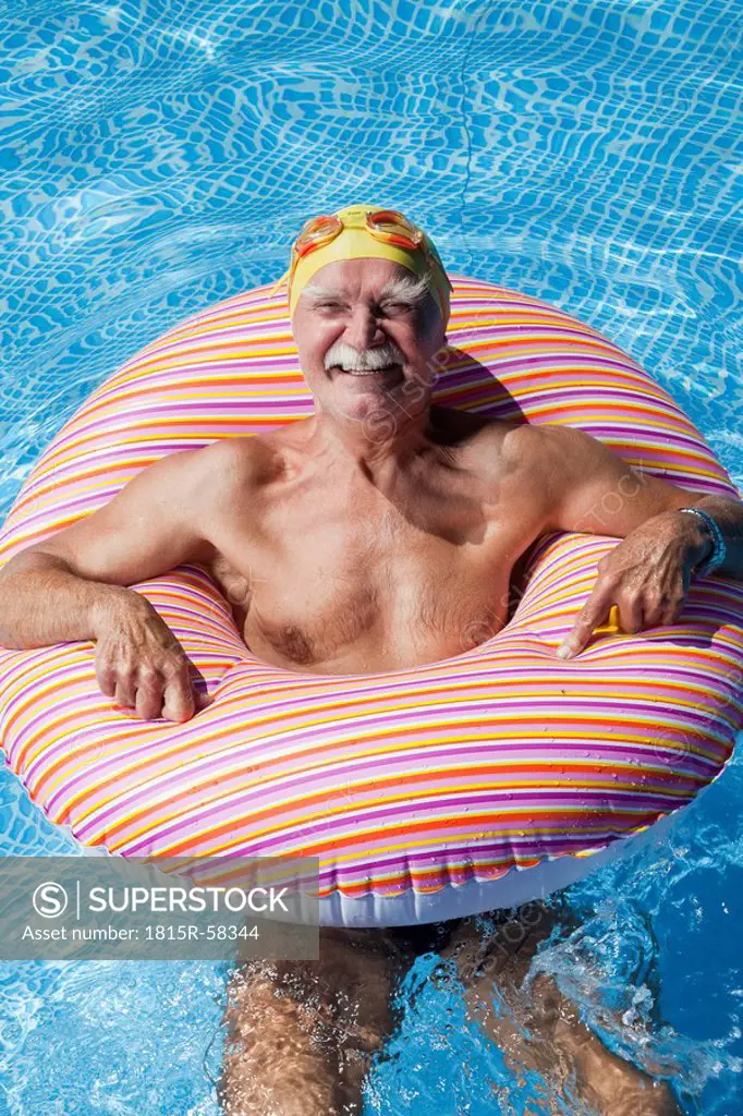 Austria, Senior man with floating tire in swimming pool, smiling, portrait
