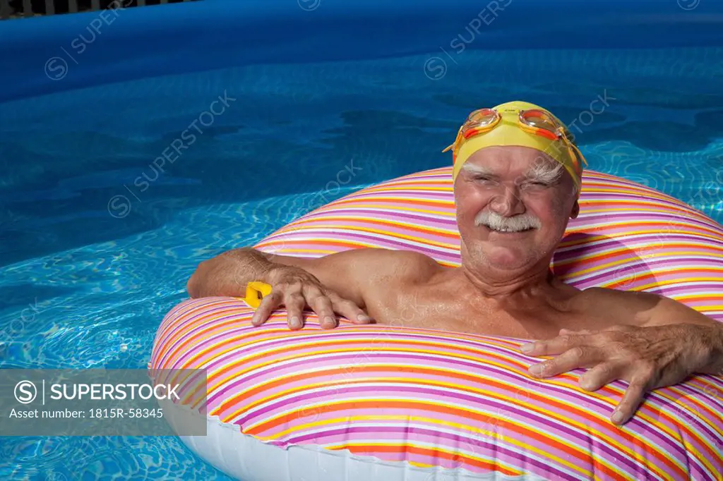 Austria, Senior man with floating tire in swimming pool, smiling, portrait