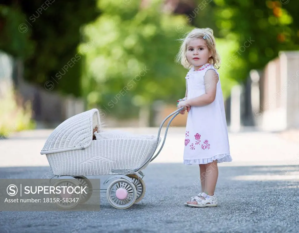 Germany, Bavaria, Girl 2_3 playing with toy baby carriage