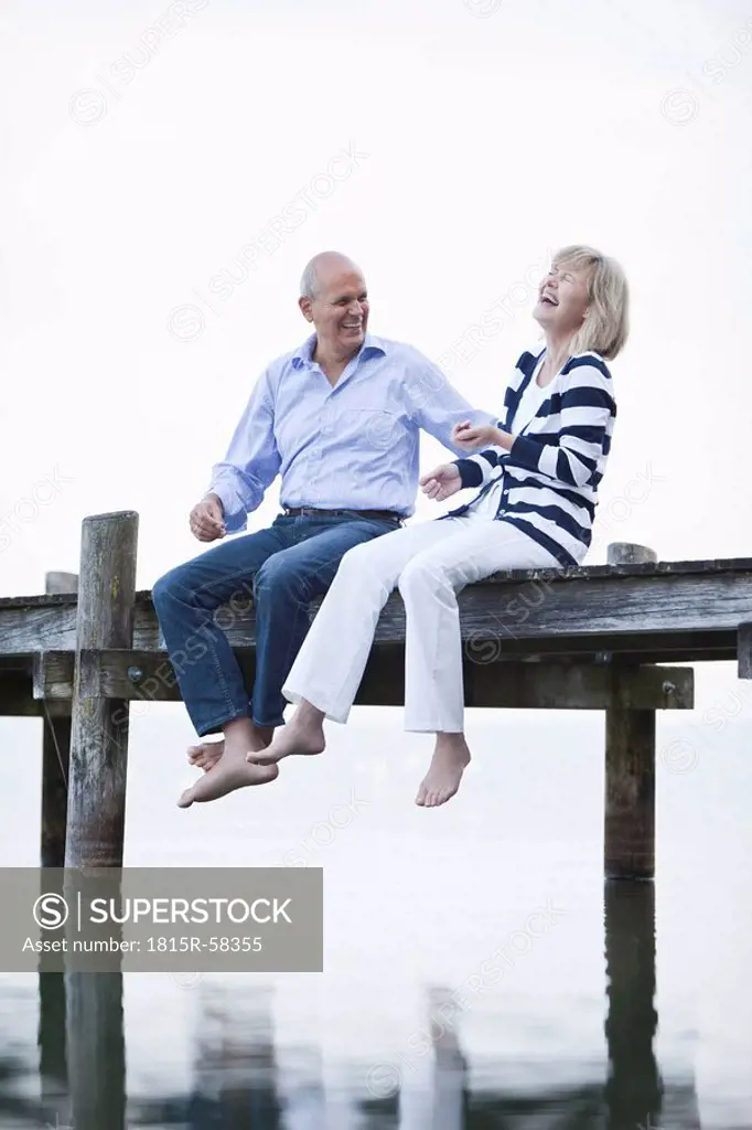 Germany, Bavaria, Starnberger See, Senior couple sitting on jetty, laughing, portrait