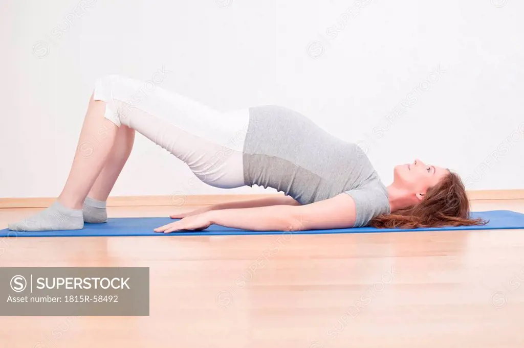 Pregnant woman practising yoga, bridge pose, side view