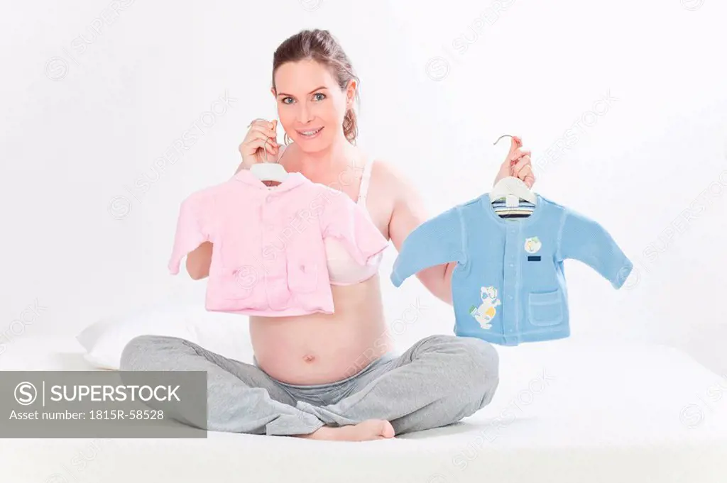 Pregnant woman holding baby clothes, smiling, portrait
