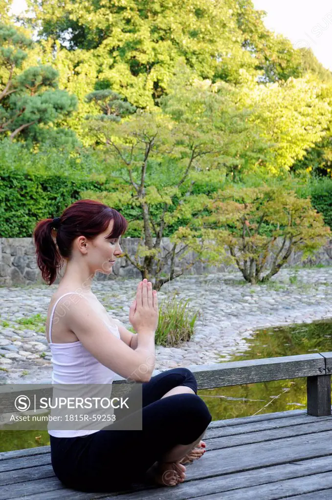 Germany, Bavaria, Munich, Young woman exercising yoga, hands folded