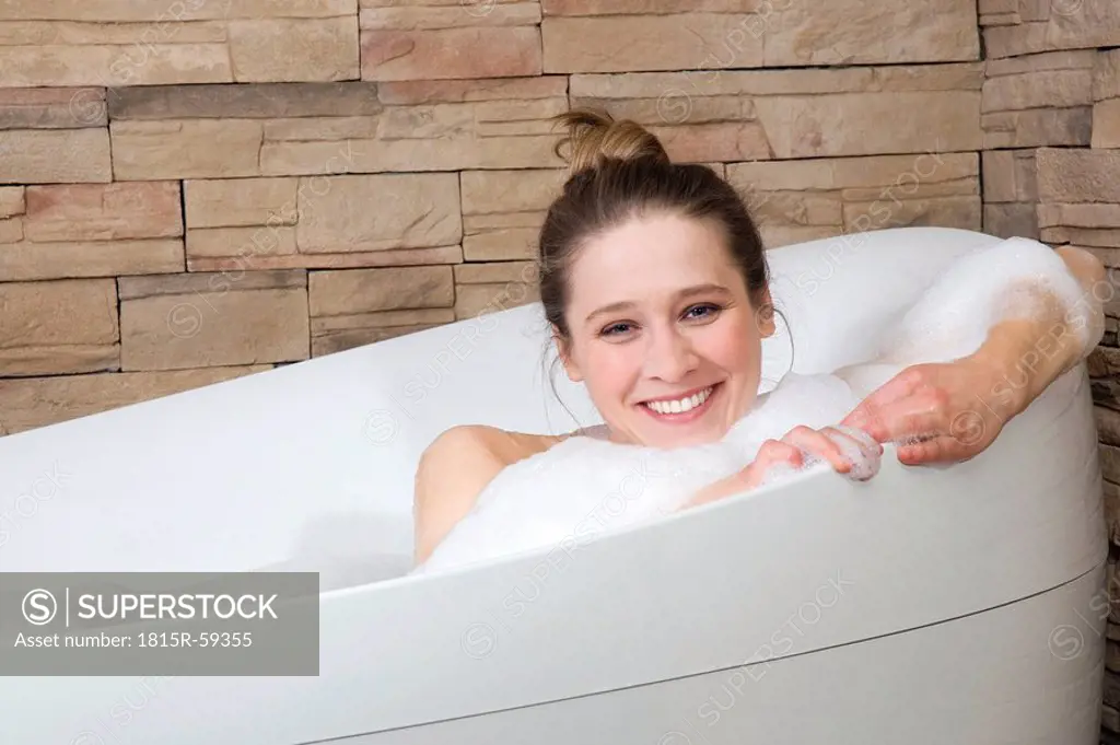 Young woman in bathtub, smiling, portrait