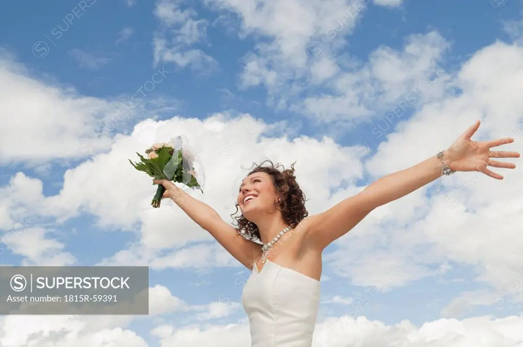 Germany, Bavaria, Smiling Bride with bouquet and arms outstreched , outdoors
