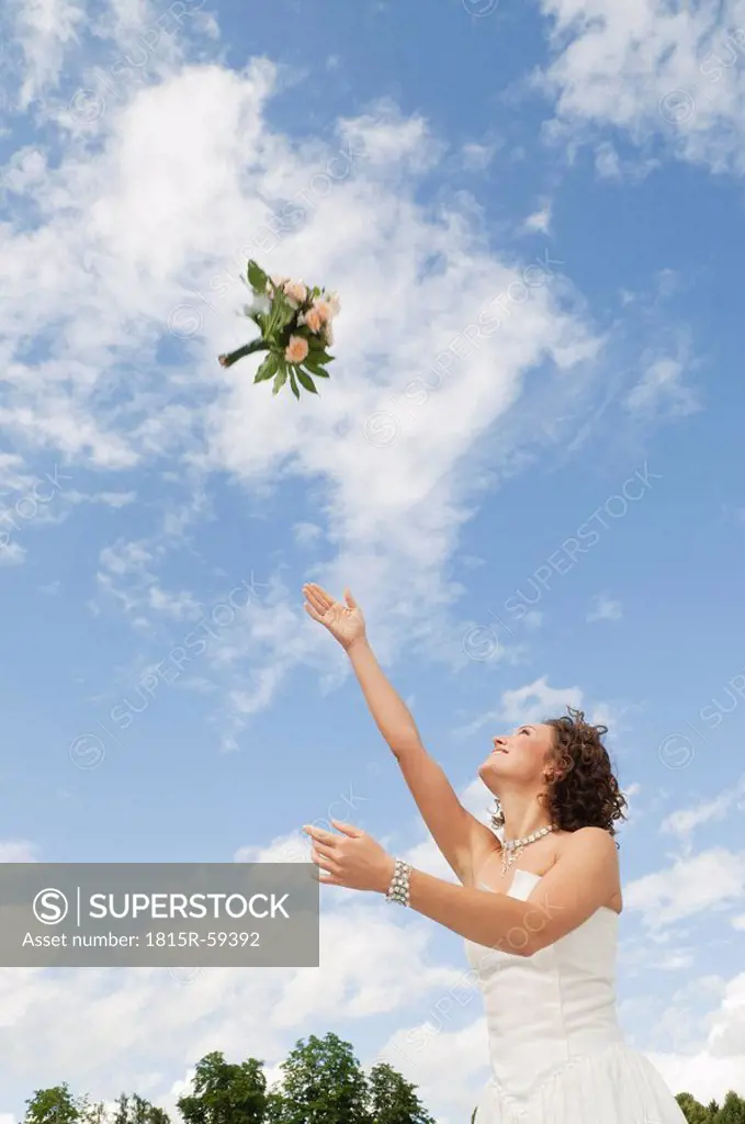 Germany, Bavaria, Young bride throwing a bouquet into the sky
