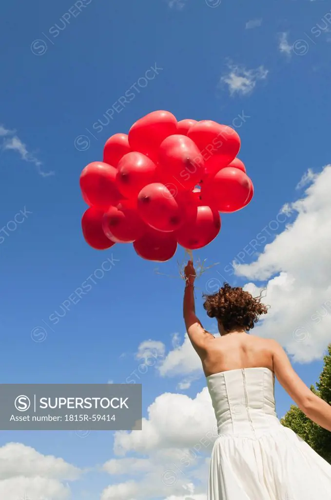 Germany, Bavaria, Bride holding red balloons, outdoors, rear view