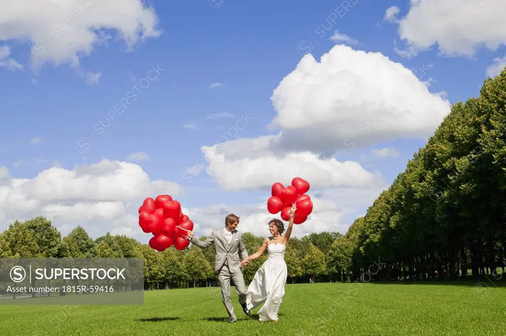 Germany, Bavaria, Bride and groom holding red balloons, outdoors