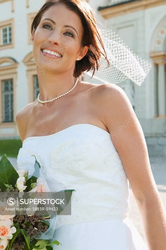 Germany, Bavaria, Bride holding bunch of flowers in front of building, portrait, close_up