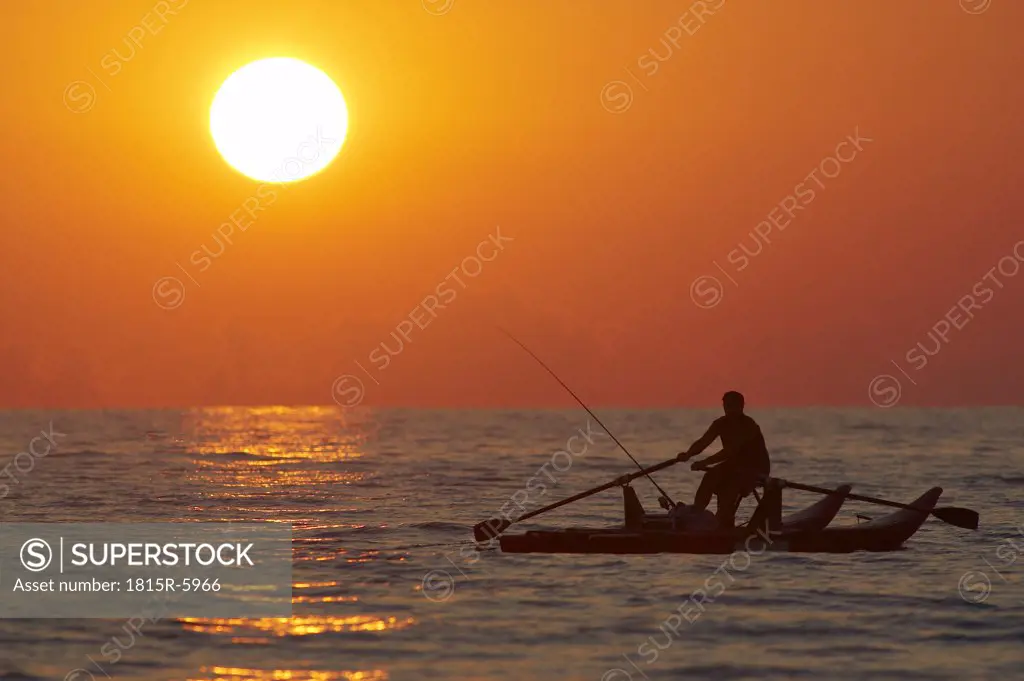 Italy, Forte dei Marmi, Man fishing in boat at sunset
