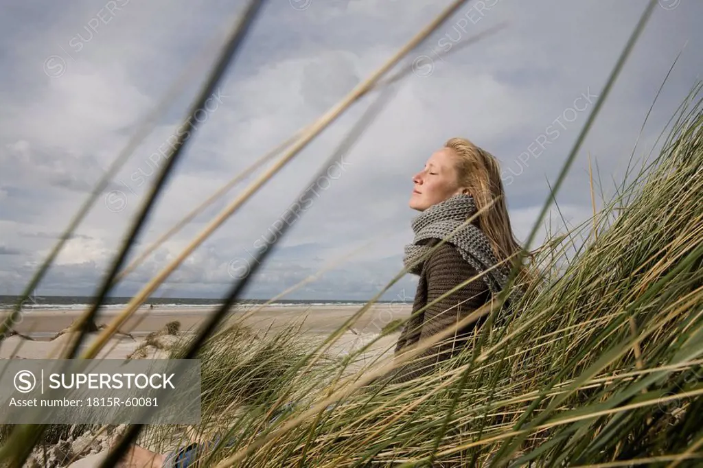 Germany, Schleswig Holstein, Amrum, Young woman on grassy sand dune, eyes closed