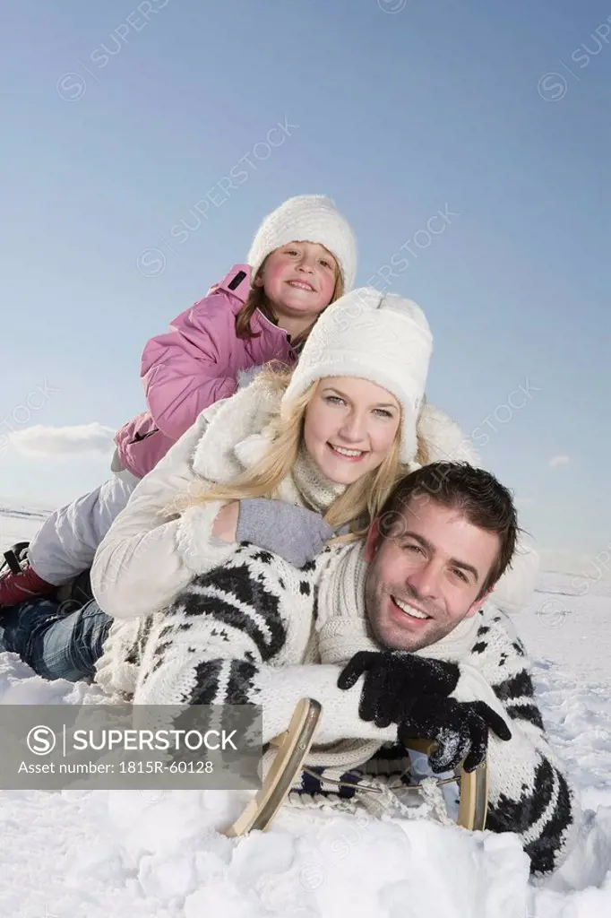 Germany, Bavaria, Munich, Family lying on sledge, smiling, portrait