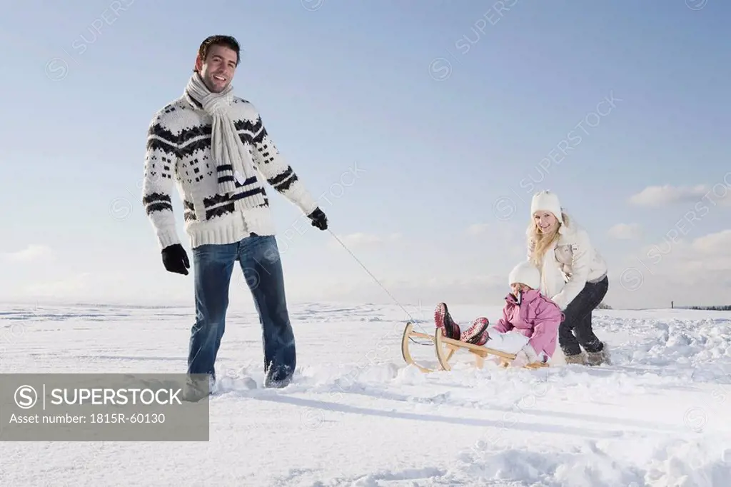 Germany, Bavaria, Munich, Father pulling girl 6_7 on sledge, Mother backing daughter