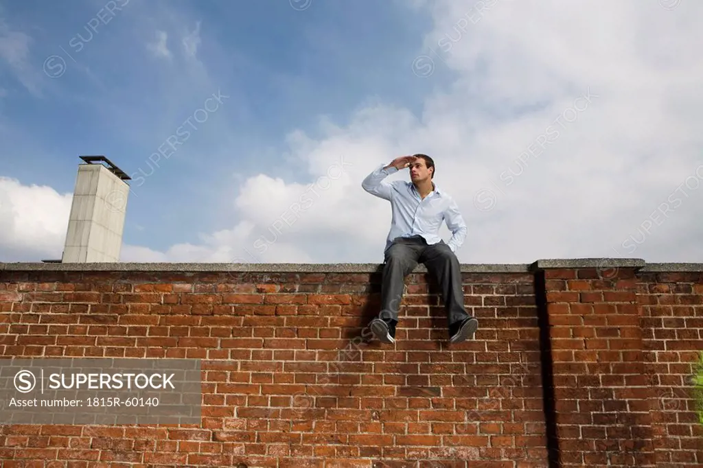Germany, Bavaria, Munich, Young man sitting on top of brick wall