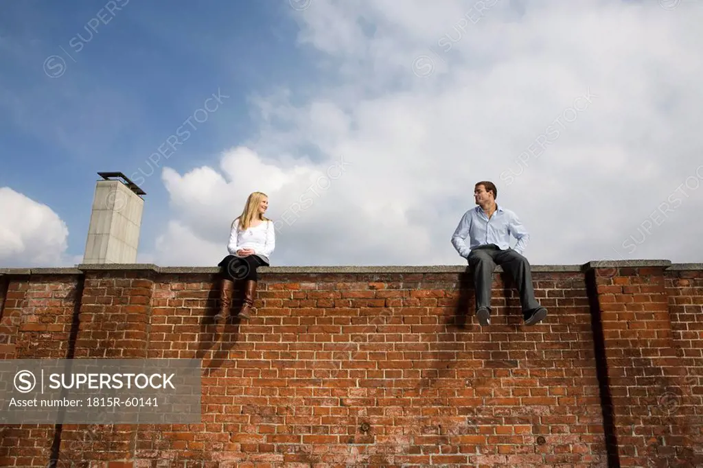 Germany, Bavaria, Munich Young couple sitting on top of brick wall