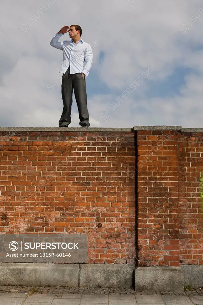 Germany, Bavaria, Munich, Young man on brick wall, watching out