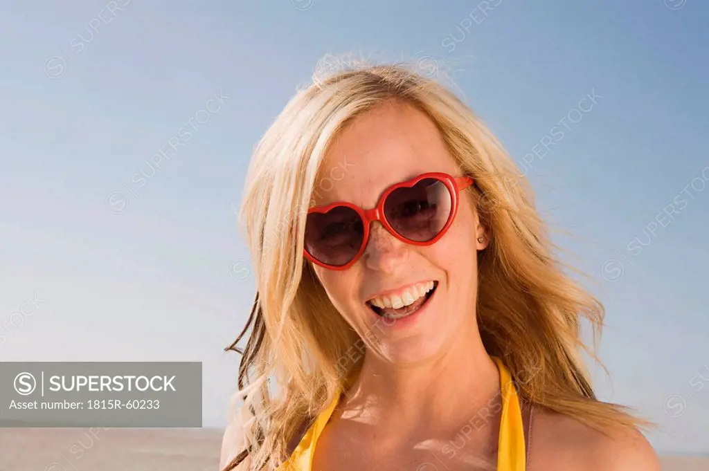 Germany, Schleswig Holstein, Amrum, Woman on beach wearing sunglasses, laughing, portrait, close_up