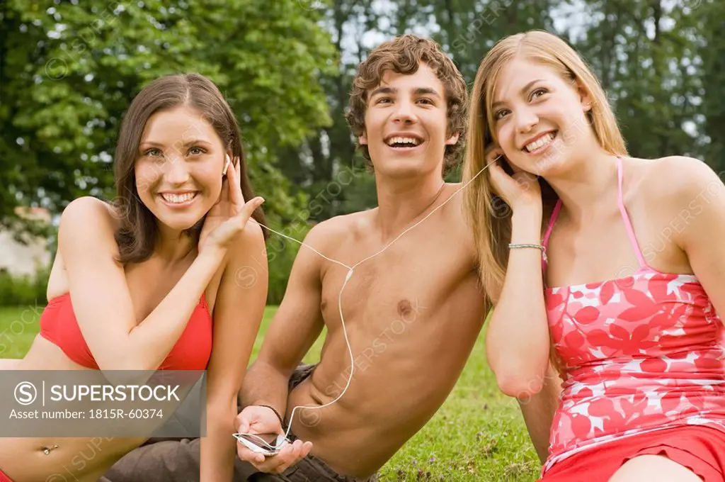 Germany, Bavaria, Starnberger See, Young people sitting on meadow listening to music, smiling, portrait, close_up