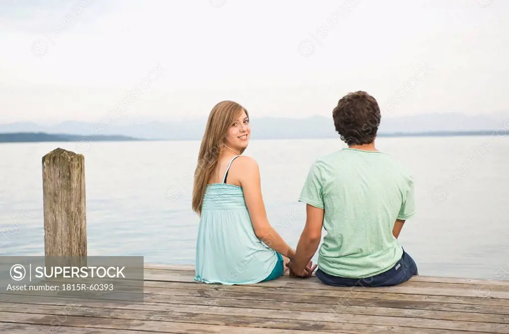 Germany, Bavaria, Starnberger See, Young couple sitting on jetty, rear view