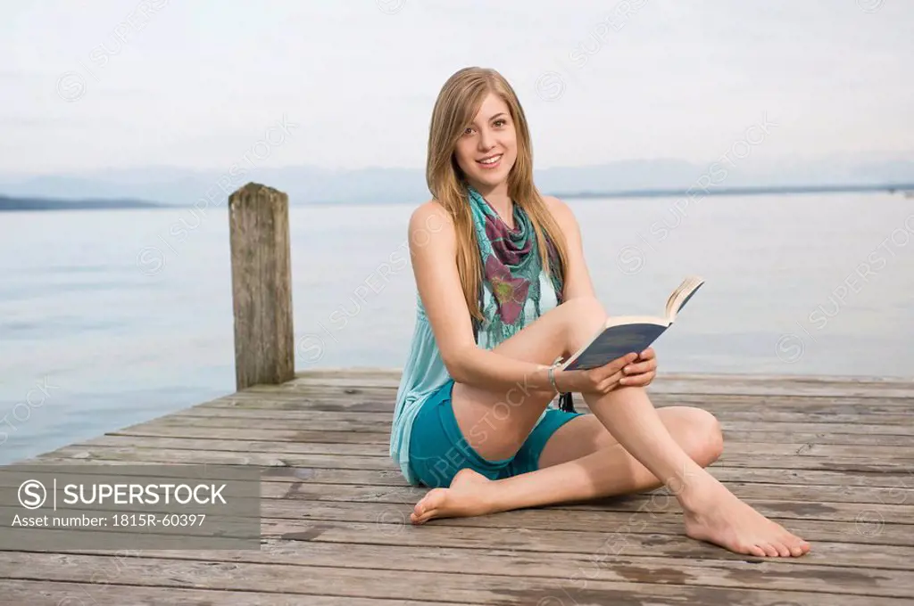 Germany, Bavaria, Starnberger See, Young woman on jetty reading book