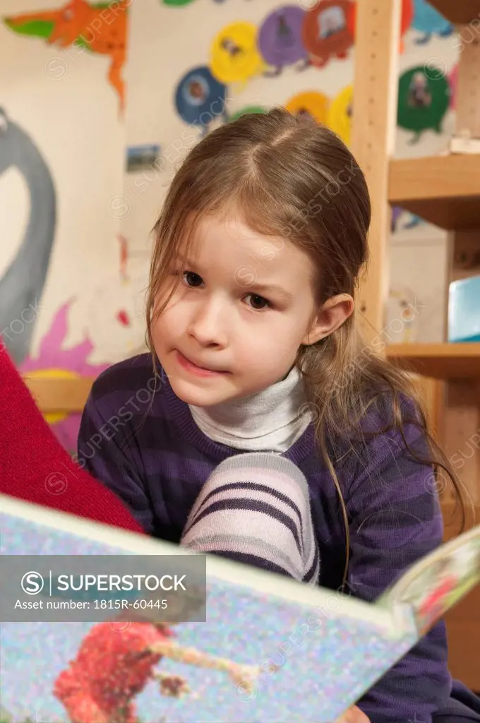 Germany, Girl 4_5 in nursery reading a book, portrait