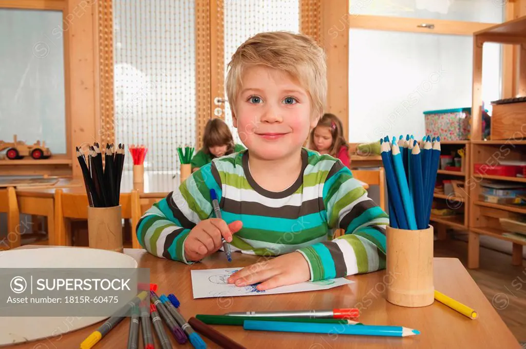 Germany, Children in nursery, boy 4_5 in foreground holding felt_tip pen, smiling, portrait