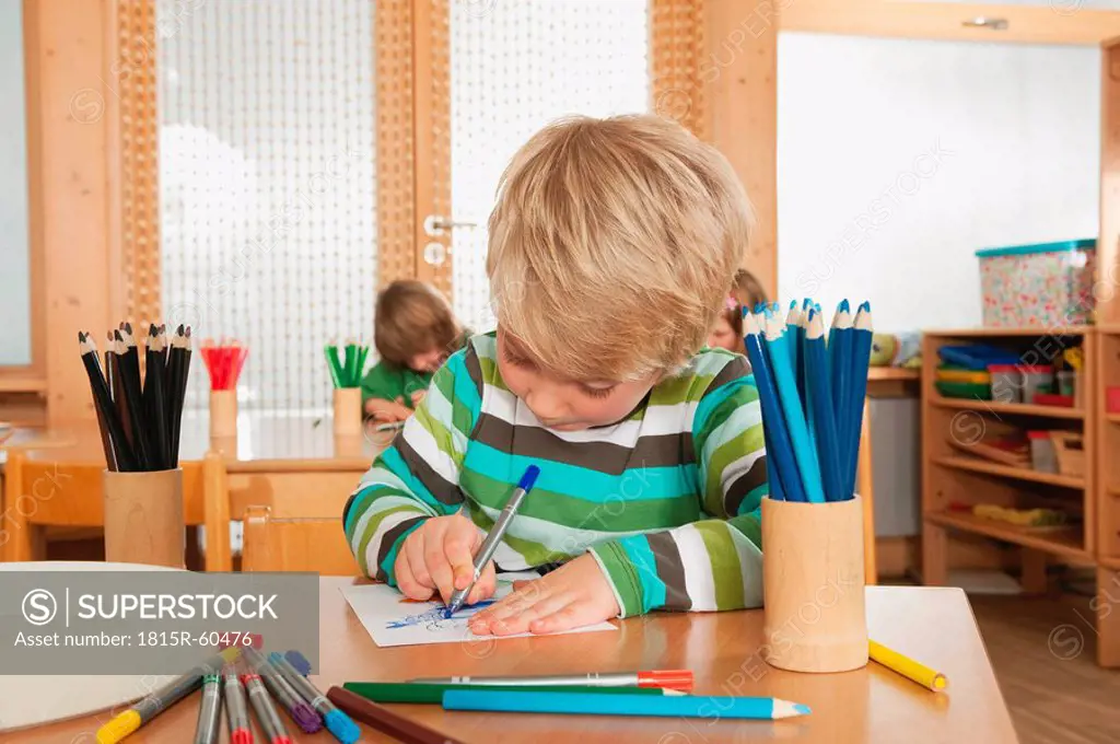 Germany, Children in nursery, boy 4_5 in foreground drawing, looking down