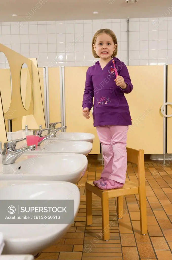 Germany, Girl 3_4 standing on chair in lavatory holding toothbrush, side view, portrait