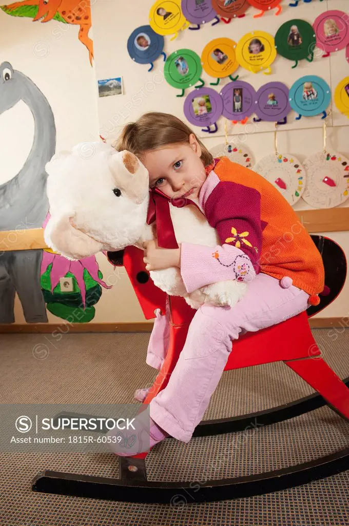 Germany, Girl 3_4 sitting on rocking horse, holding teddy, portrait