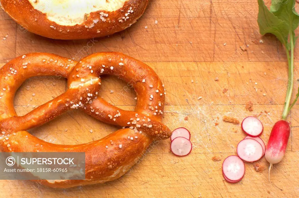Pretzel and slices of red radish on wooden board, elevated view
