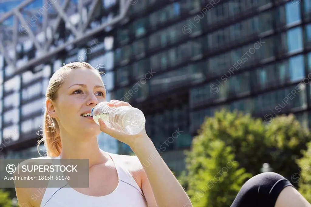 Germany, Berlin, Young woman drinking water from bottle, building in background, portrait