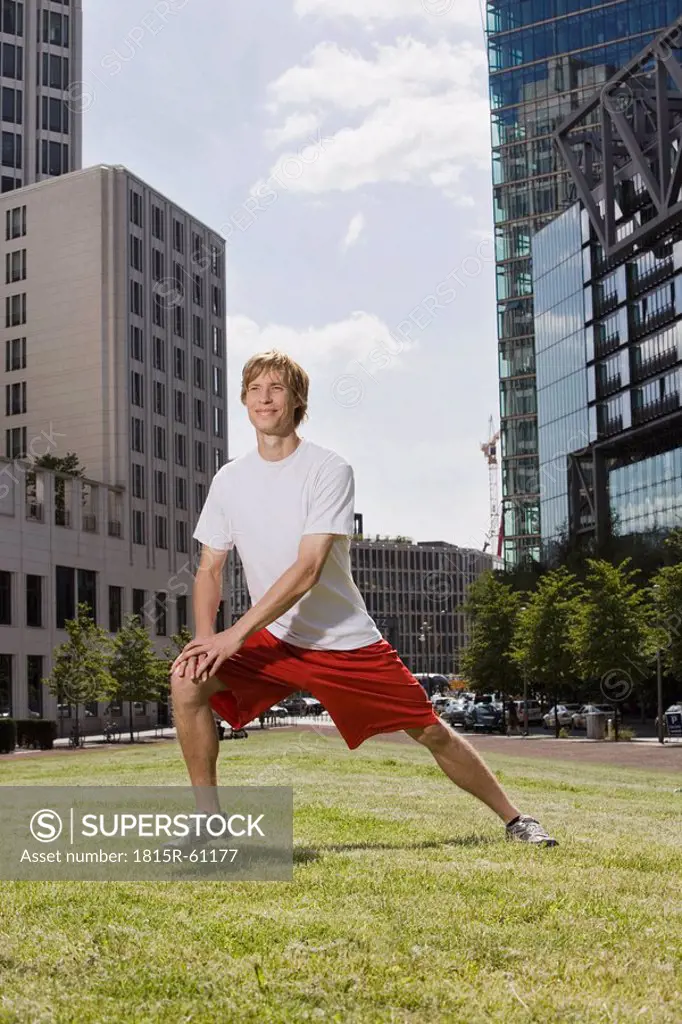 Germany, Berlin, Young man stretching on lawn