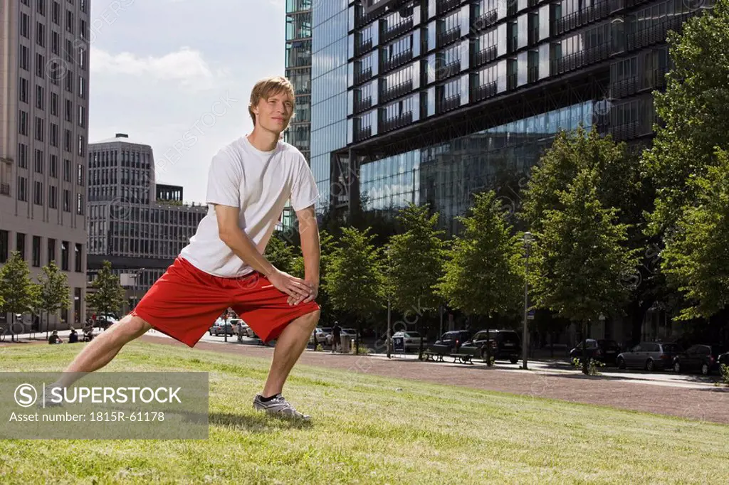 Germany, Berlin, Young man stretching on lawn