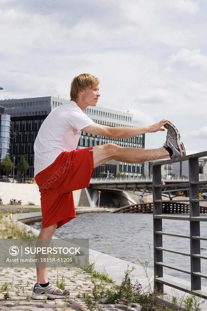 Germany, Berlin, Young man stretching leg on railing