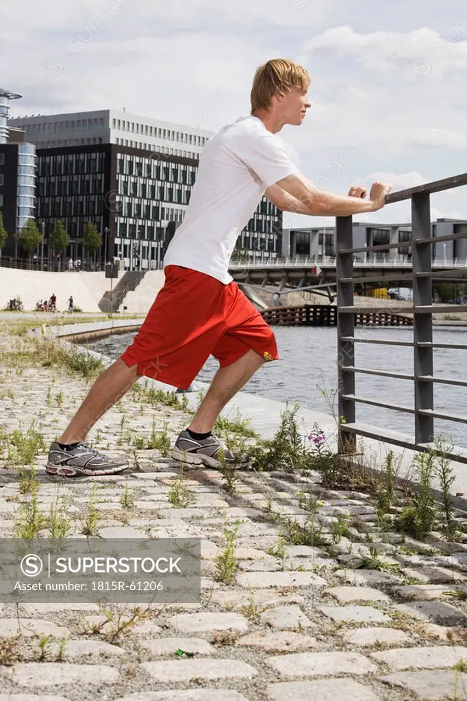 Germany, Berlin, Young man stretching on railing