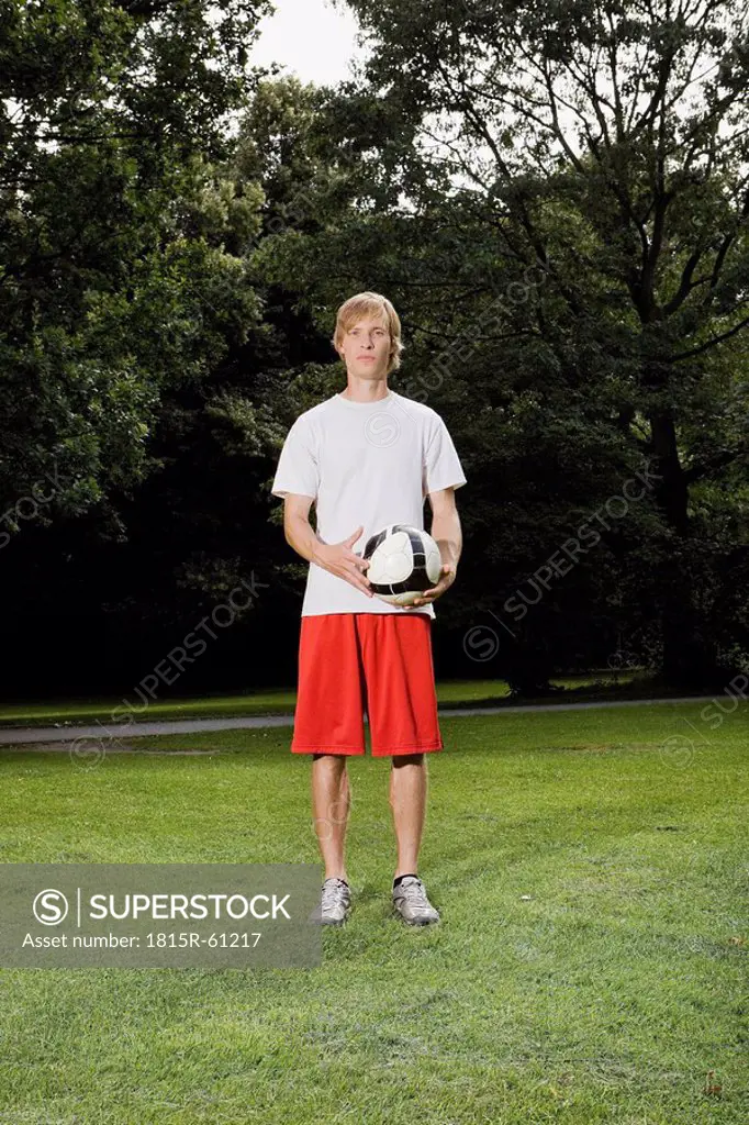 Germany, Berlin, Young man on lawn holding soccer ball, portrait