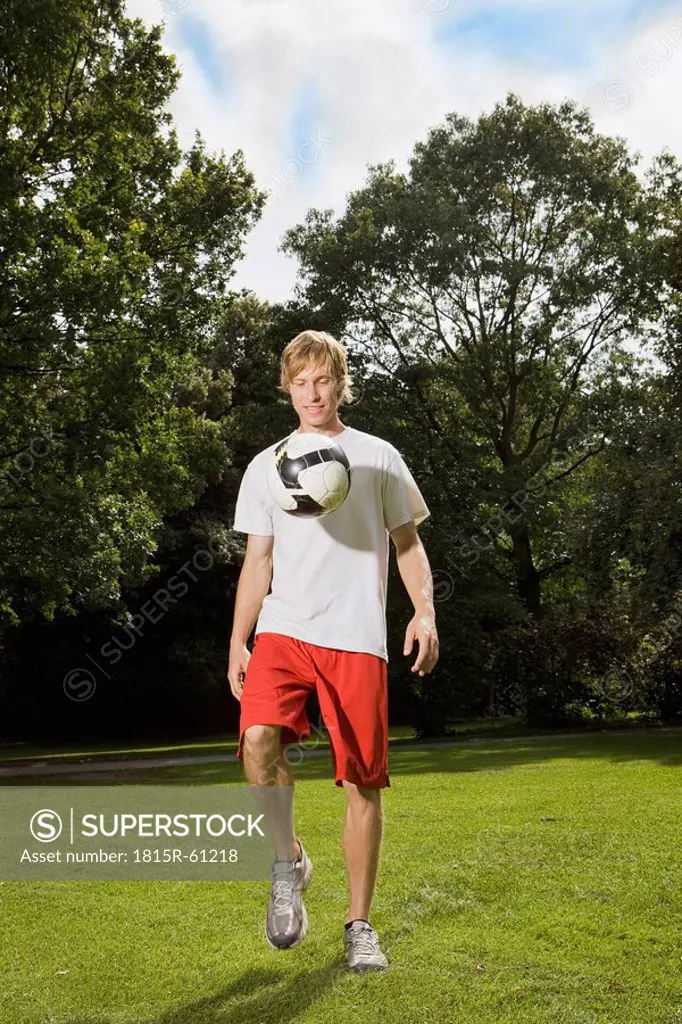 Germany, Berlin, Young man on lawn playing with soccer ball