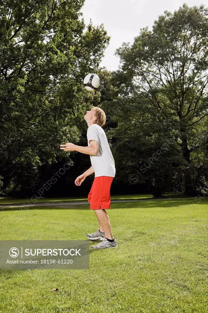 Germany, Berlin, Young man on lawn playing with soccer ball