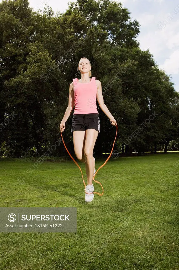 Germany, Berlin, Young woman in park jumping rope