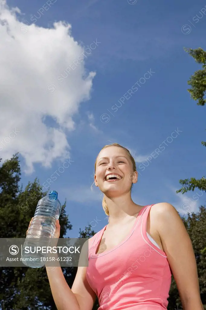 Germany, Berlin, Young woman holding water bottle, laughing, portrait