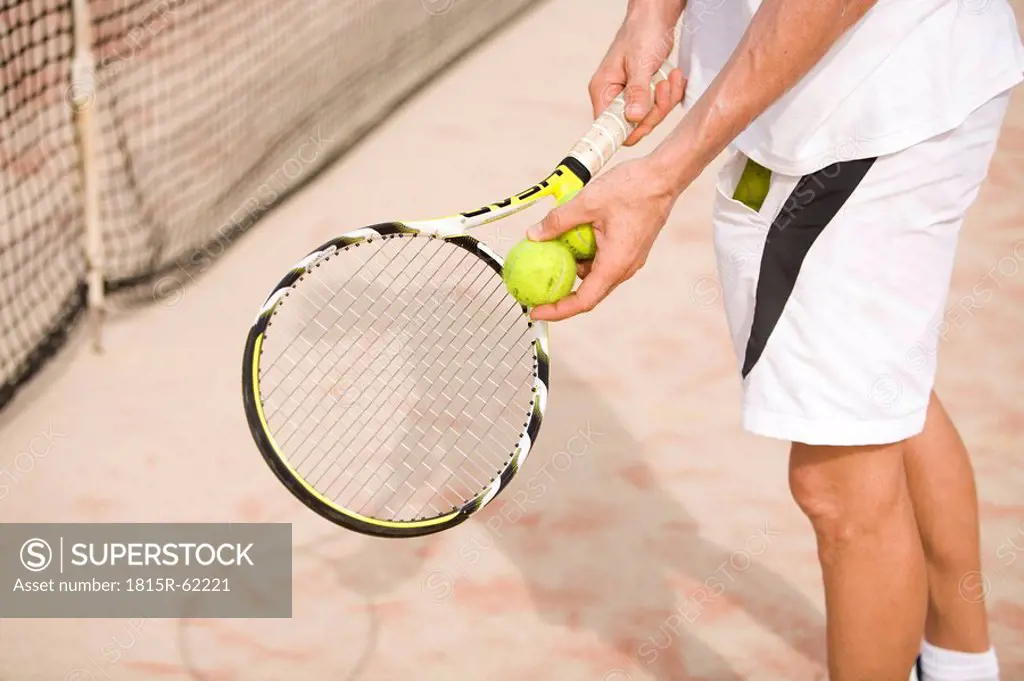 Male tennis player holding tennis racket, low section