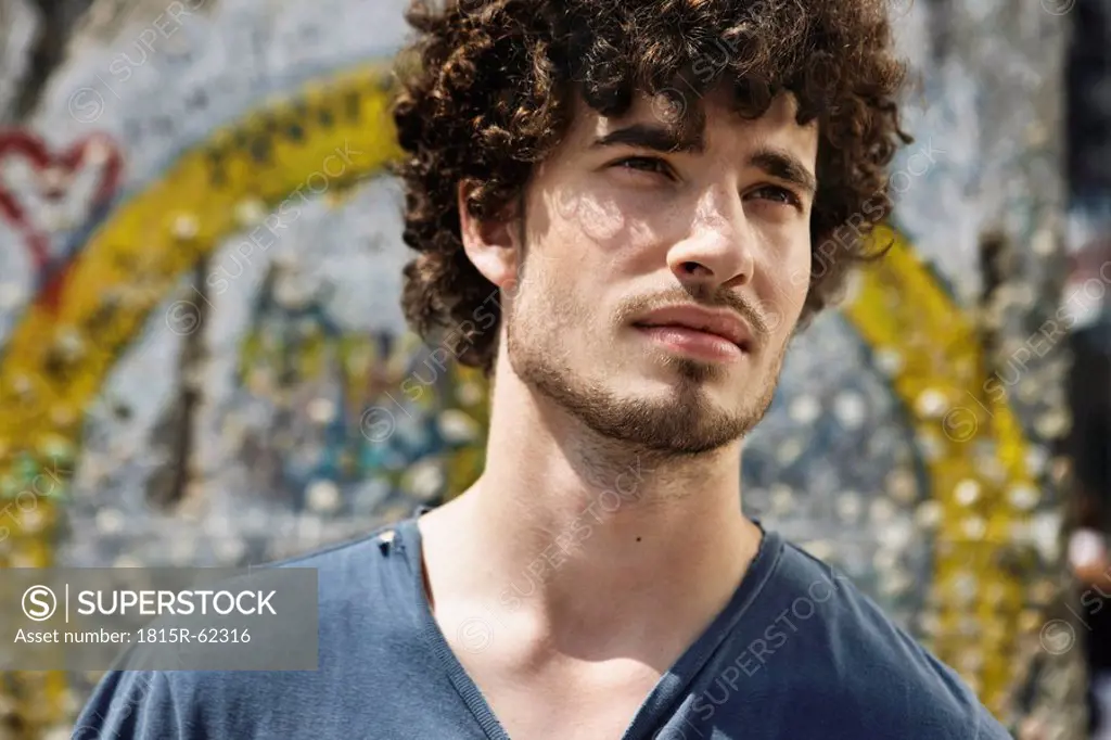Germany, Berlin, Young man standing in front of wall with graffiti, portrait, close_up