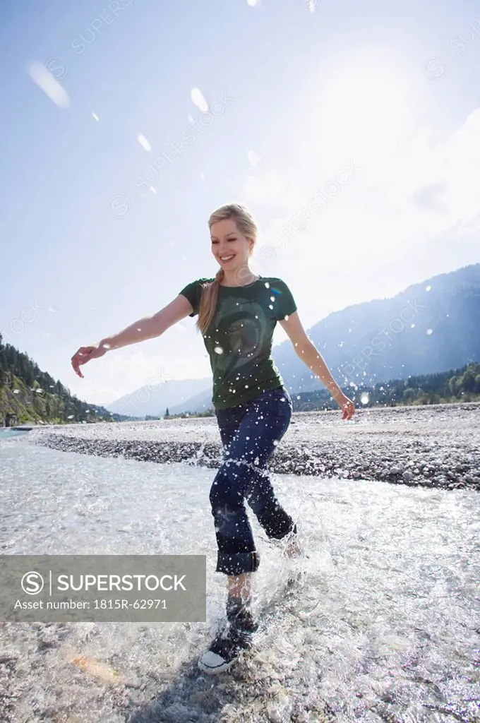Germany, Bavaria, Tölzer Land, Young woman running through river, smiling