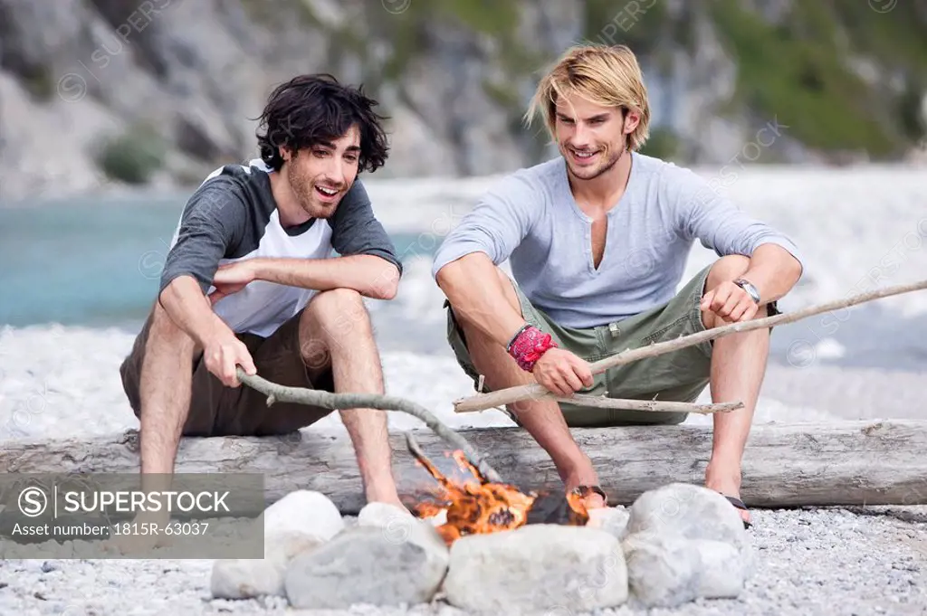 Germany, Bavaria, Tölzer Land, Men sitting at campfire near river